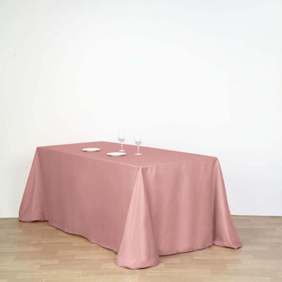 Pink tablecloth draped over a table with plates and glasses on a plain background.