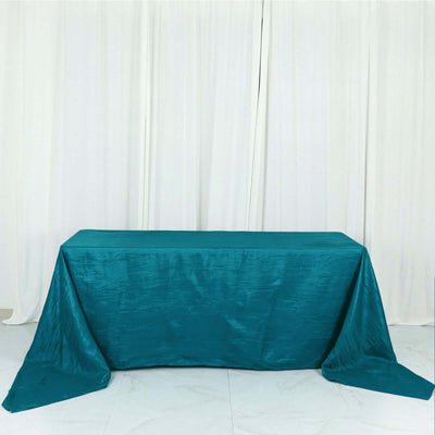 Teal tablecloth draped over a rectangular table on a plain backdrop.