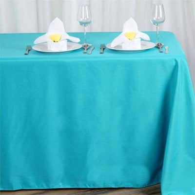 Turquoise tablecloth set with elegant napkin folds and dining utensils.