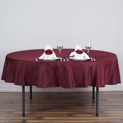 Elegant round table set with burgundy tablecloth and rose-adorned napkins.