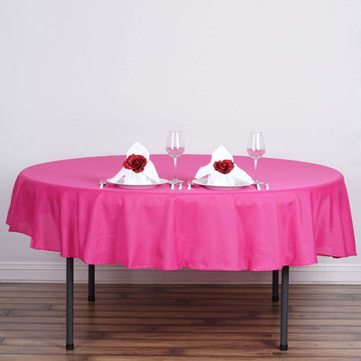 Pink round tablecloth on a dining table set for two with decorative napkins.
