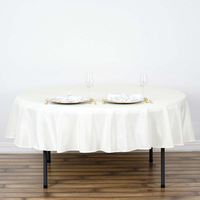 Round white tablecloth draped over a table set for two with glassware and plates.