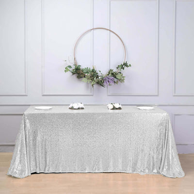 Silver sequin tablecloth draped over a table with a floral wreath backdrop.
