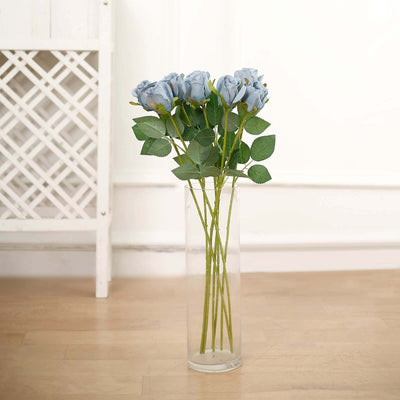Blue roses in a glass vase on a wooden floor.