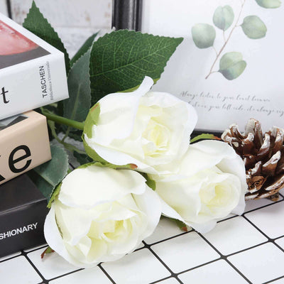 White artificial roses with green leaves on a decorative surface.