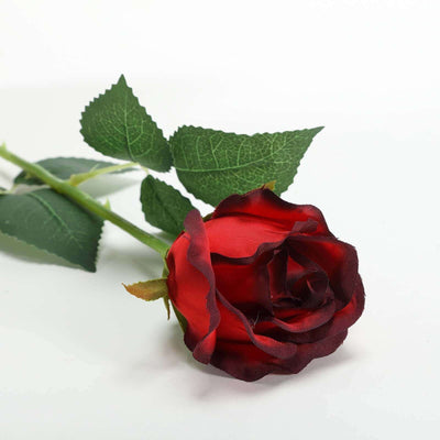Red silk rose with green leaves on a plain white background.
