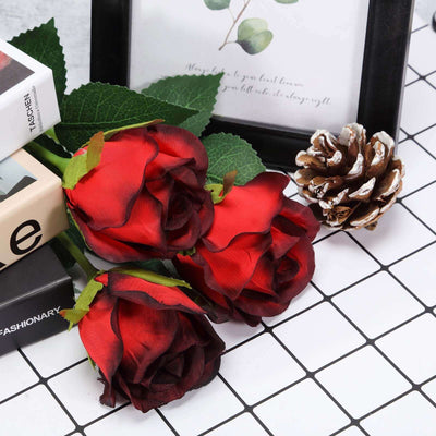 Red artificial roses with greenery, displayed with decorative items on a grid background.