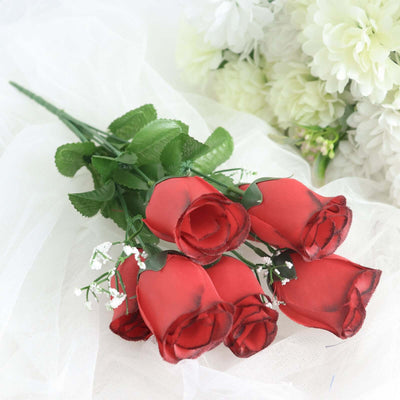 Red artificial roses bouquet with green leaves on a soft white background.