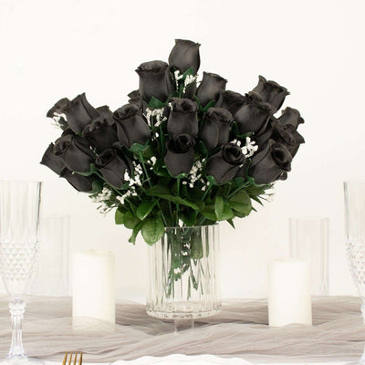 Black rose bouquet in a clear vase on a table with candles and crystal glasses.