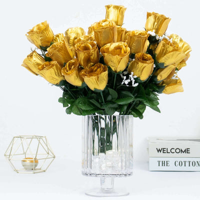 Gold artificial roses in a clear vase with decorative stones.