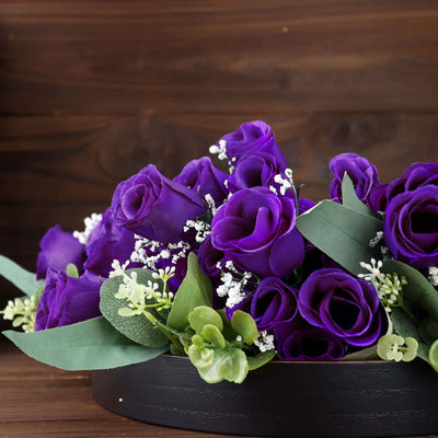 Purple roses arrangement with greenery in a decorative bowl.