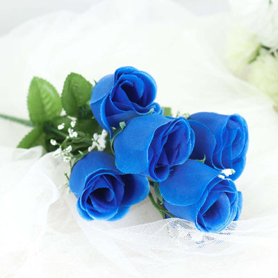 Blue artificial rose bouquet with green leaves on soft white fabric.