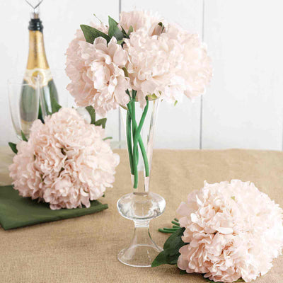 Pink peony flowers in a clear vase on a table setting.