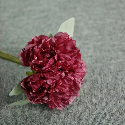 Artificial red carnation bouquet on textured surface.