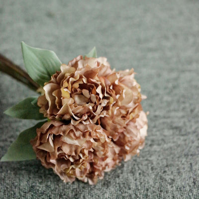 Artificial peach peony bouquet with green leaves on a textured background.