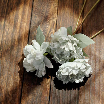 Artificial peony flowers in soft white with green leaves on wooden background.