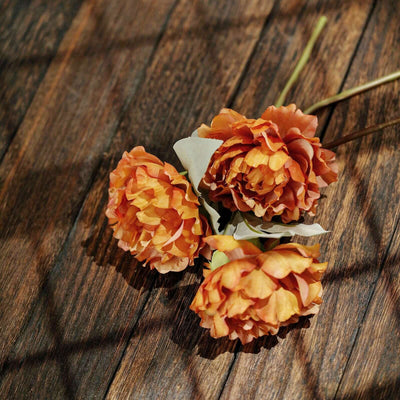 Three artificial orange flowers on a wooden surface.