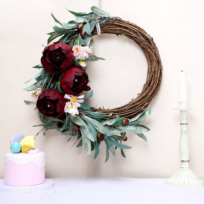 Floral wreath with red roses and daisies, styled with a cake and candle.
