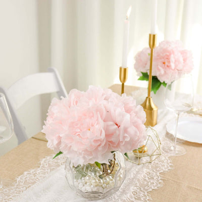 Pink peony floral arrangement in a glass vase with pearls on a dining table.