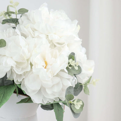 White peony bouquet with green leaves in a modern vase.