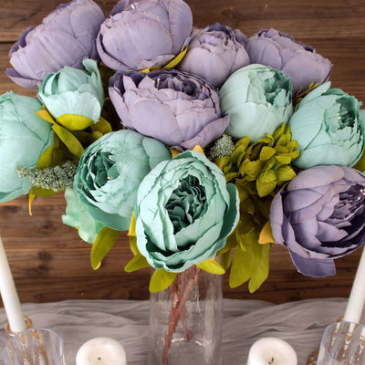 Artificial peony bouquet in shades of purple and teal, styled in a glass vase.