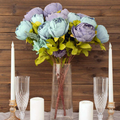 Artificial peony bouquet in a clear vase with candles and glasses