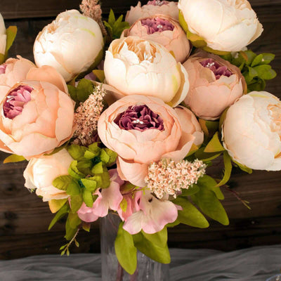 Peach and white peony bouquet with greenery in a clear vase.