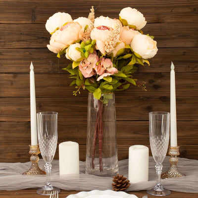 Elegant floral arrangement with peonies in a clear vase on a rustic table setting.