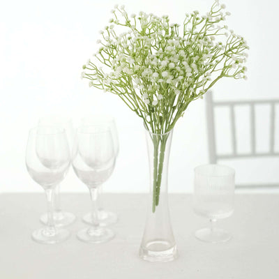 Clear vase with white flowers, surrounded by glassware on a table.