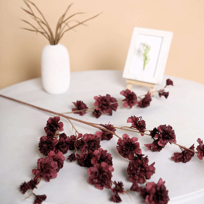 Dried burgundy flowers on a marble table with a vase and framed art.