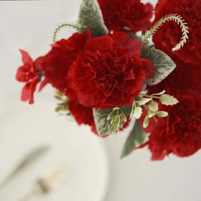 Red carnation bouquet with green foliage against a plain backdrop.