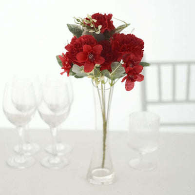 Red flower bouquet in a clear vase with glassware in the background.