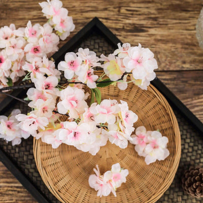 Pink cherry blossom branches arranged on a woven tray.