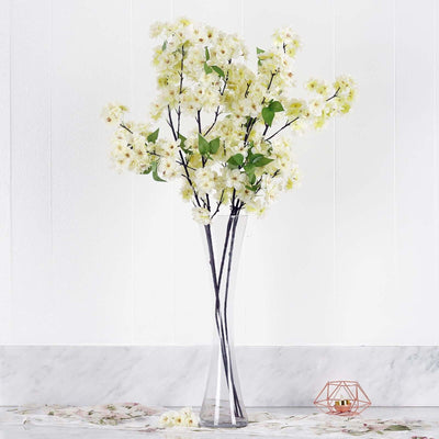 Artificial white flower arrangement in a clear vase on a marble surface.
