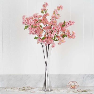 Pink artificial cherry blossom bouquet in a clear vase.
