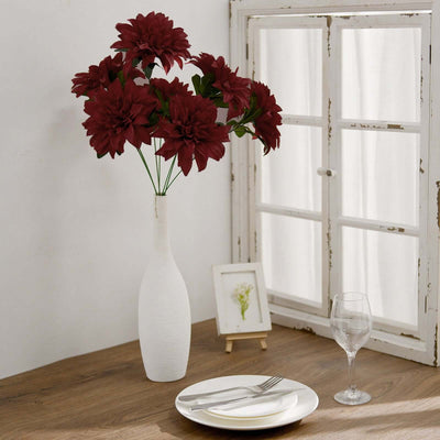 Red flower arrangement in a stylish white vase on a wooden table.