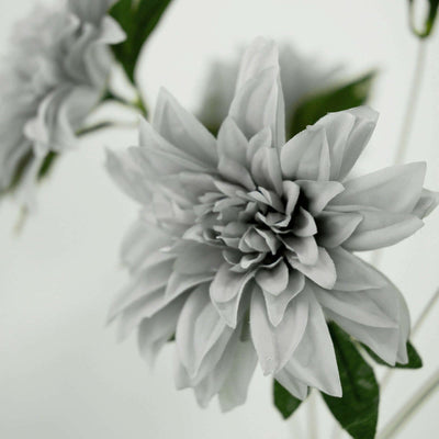 Gray artificial flower with detailed petals and green leaves.