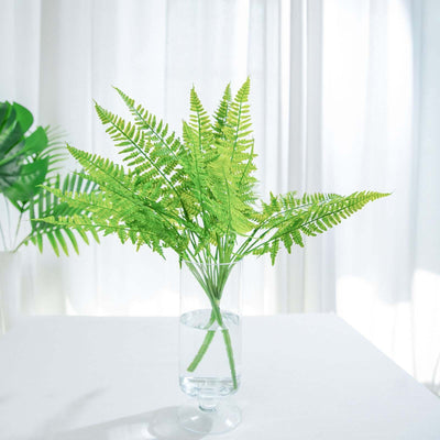 Green fern arrangement in a clear vase on a light background.