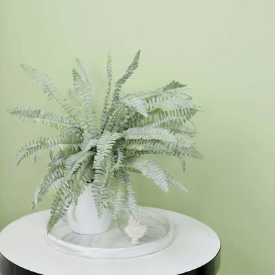 Artificial fern plant in white pot on a marble table.