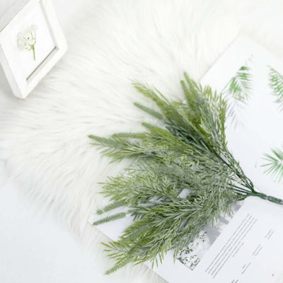 Green foliage branch on a soft white surface with a photo frame.