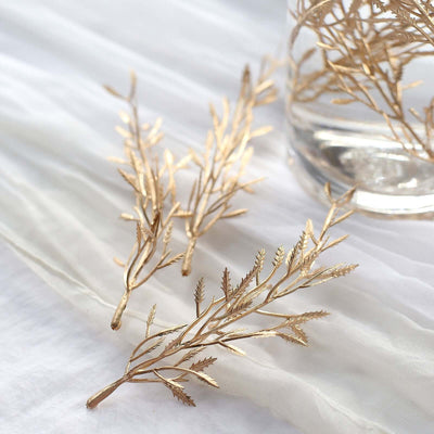 Gold leaf branches arranged near a glass vase on a soft fabric background.