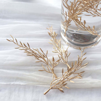 Gold leaf branches beside a glass vase with water.