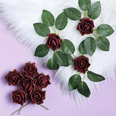 Artificial burgundy roses with green leaves on a soft purple background.