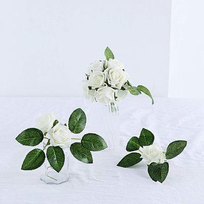 White artificial roses in clear vases with green leaves.