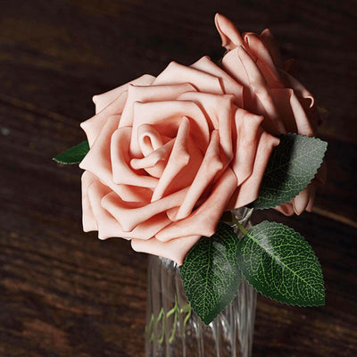 Peach silk roses in a glass vase with green leaves.