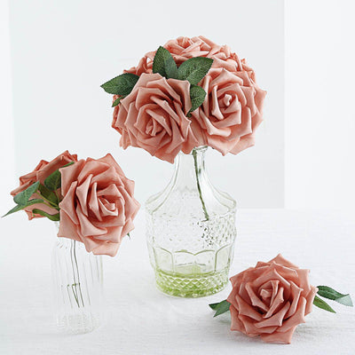 Pink artificial roses in glass vases on a white table.