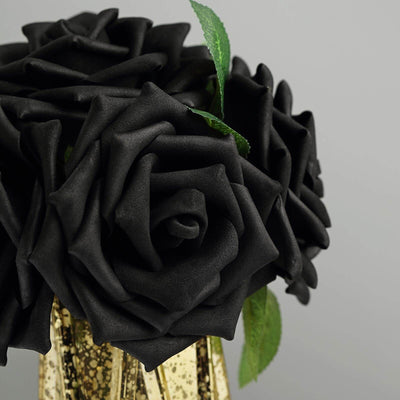 Black faux roses in a gold vase against a grey background.
