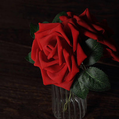 Red artificial roses in a glass vase against a dark wooden background.