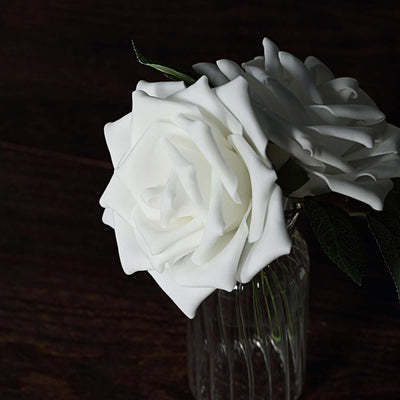 White artificial roses in a glass vase on a dark wooden surface.