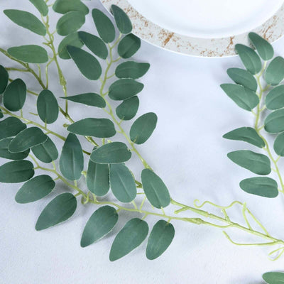 Green artificial leaves on a white tablecloth with a decorative plate.